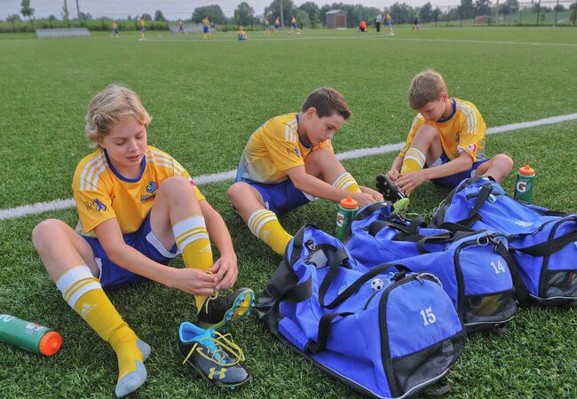 three young soccer players tying up their cleats for a big game on the beautifully manicured soccer pitch